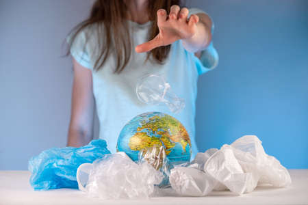 Woman is throwing the plastic on the Earth in the form of a globe that is in a pile of garbage. Concept of environmental pollution and saving the planetの写真素材