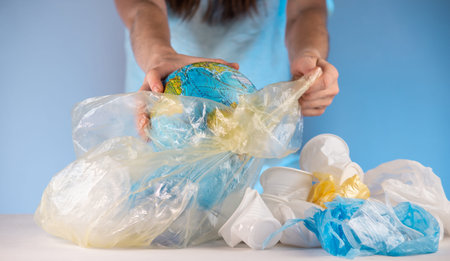 A woman is putting Earth in the form of a globe in a garbage bag with plastic. Concept of...