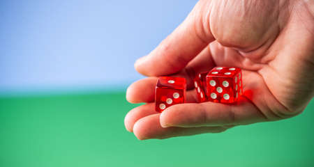 A hand is holding red dice over a green tableの写真素材