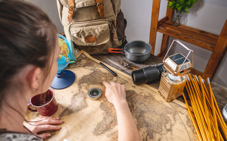 A woman is looking at a map of the world and chooses a place for her next trip on a wooden table...
