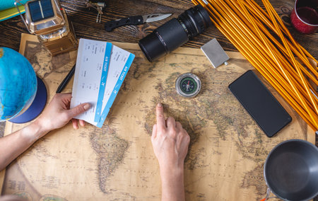 A woman is choosing a place for her next trip by pointing to a map of the world on a wooden table...
