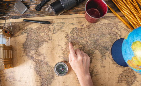 A woman is looking at a map of the world and chooses a place for her next trip on a wooden table...