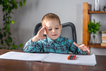 Cute child boy draws with chalk on paper in an album at the table. Concept of preschool education...