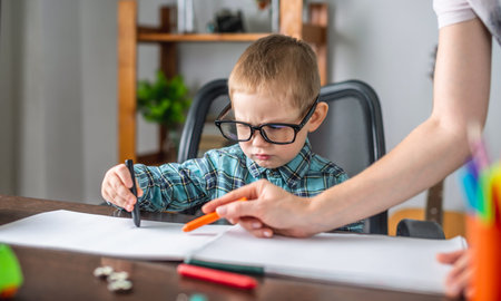 Mom is helping cute child to draw with pencils on paper in an album at the table. Concept of...
