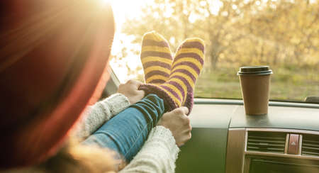 Woman in a car in warm woolen yellow socks on the car dashboard. Cozy autumn weekend trip. The concept of freedom of travelの写真素材