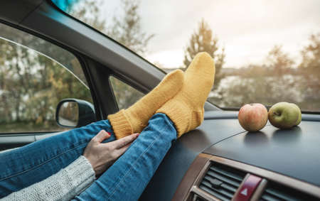 Woman in a car in warm woolen yellow socks on the car dashboard. Cozy autumn weekend trip. The concept of freedom of travelの写真素材