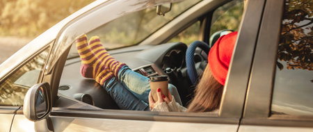Woman in a car in warm woolen socks yellow is holding a Cup of coffee in hands at sunset. Cozy...