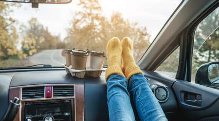 Woman in a car in warm woolen yellow socks is holding a Cup of coffee in hands. Cozy autumn weekend trip. The concept of freedom of travelの写真素材