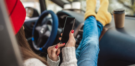 Woman in a car in warm socks is holding a mobile phone gadget and cup of coffee. Cozy autumn weekend...