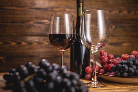 A bottle of dry red wine with a glass and a bunch of grapes on a wooden table. Concept of viticulture and winemakingの写真素材