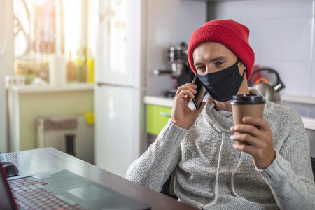 A young man in a black face mask is using a phone. Concept of remote work, distance communication...