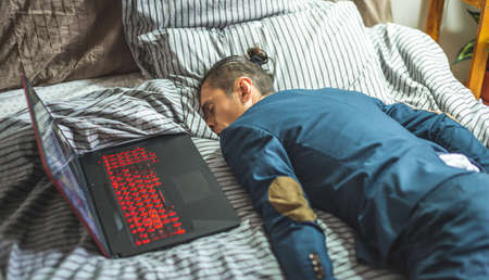 A business man in a suit sleeps in a bed next to a laptop and phone during the day. The concept of fatigue and exhaustion from hard workの写真素材