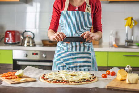 A female chef blogger takes photos of home-made pizza on her phone. The concept of food photography for social networksの写真素材