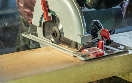 Worker carpenter is sawing a wooden Board with a hand-held circular saw. Closeup.の写真素材