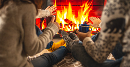 Man and woman are sitting next to the fireplace, which is depicted on the TV screen and drinking a hot beverage. Concept of creating a cozy winter atmosphere at homeの写真素材