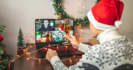A man in a red Santa hat with a glass of champagne is remotely communicating with friends and family via video link. Concept of Christmas and New Year parties onlineの写真素材