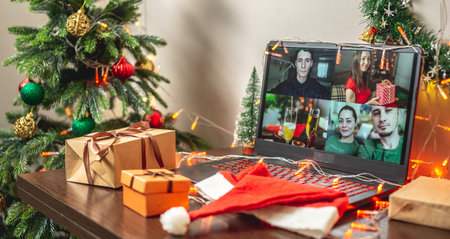 There are gift boxes, Santa's red hat and a computer with video chat on the table. Concept of celebrating New year and Christmas with family and friends remotelyの写真素材