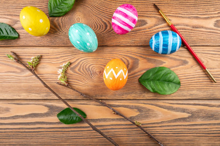 Cute Easter eggs decorated handmade with paint and paintbrush on a wooden background with green leaves and young branchesの写真素材