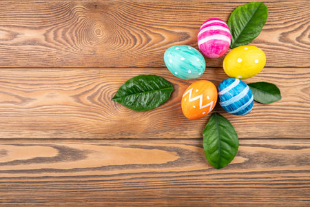 Cute Easter eggs decorated handmade with paint and paintbrush on a wooden background with green...