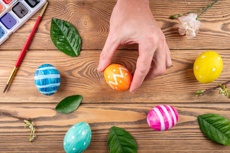 Hand is holding a cute orange egg decorated with paints next to other colorful eggs. Concept of...