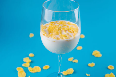 Milk in a glass and scattered yellow cornflakes on a blue background