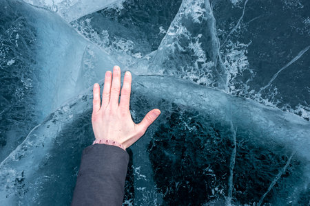 A woman's hand touches the clear blue cracked ice of Lake Baikal. Top viewの写真素材