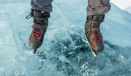 Feet in skates on the beautiful blue cracked ice of a frozen lake. Top view