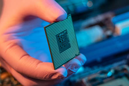 The engineer's gloved hand is holding the CPU chip against the background of the motherboard. Concept of high-tech hardware microelectronicsの写真素材