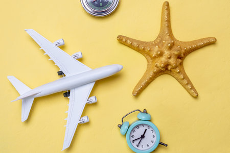 Miniature of an airplane, a golden starfish and a compass on a yellow background, top view. Concept of summer vacations and plane travelの写真素材