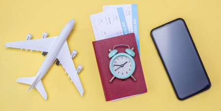 Miniature of an airplane, airline tickets with a passport and an a watch on a yellow background. Concept of time for travelの写真素材