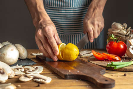 Chef in a blue apron is cutting a lemon with a knife to prepare a delicious dish. Concept of the cooking process.の写真素材
