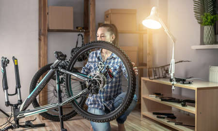 Young woman fixing a mountain bike in a workshop. Concept of preparation for the new season, repair and maintenanceの写真素材
