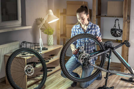 Young woman fixing a mountain bike in a workshop. Concept of preparation for the new season, repair and maintenanceの写真素材