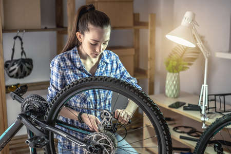 A woman in the workshop is disassembling his bike and repairing it. Concept of maintenance and preparation for the new seasonの写真素材