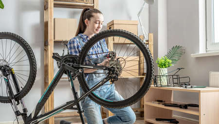A woman in the workshop is disassembling his bike and repairing it. Concept of maintenance and preparation for the new seasonの写真素材
