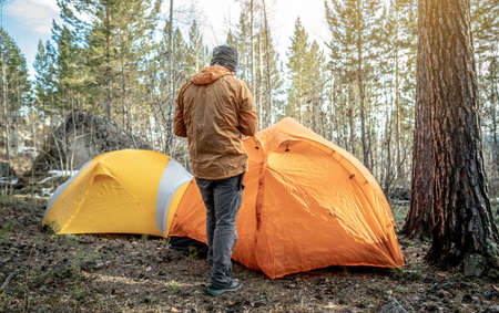 A male traveler is standing in the forest near the tents in a tent camp. Concept of hiking, spending time in nature.の写真素材