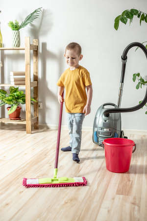 A little boy is cleaning the floor of a room using a mop. Concept of independence, help to parents, housework of the childの写真素材