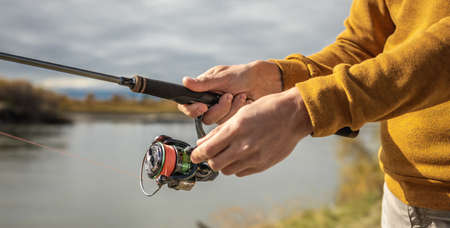 Male hands of a fisherman are holding a spinning closeup. Concept of fishing in the autumn forest, outdoor recreation, pastime, hobbyの写真素材
