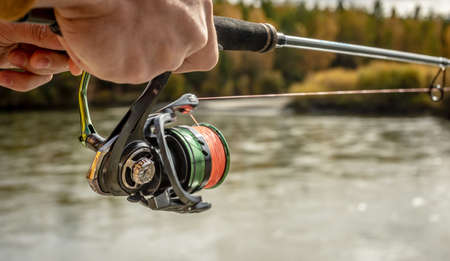 Male hands of a fisherman are holding a spinning closeup. Concept of fishing in the autumn forest, outdoor recreation, pastime, hobbyの写真素材
