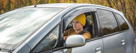 Man in yellow hat and sweater is driving a car along the autumn forest road. Concept of nature, travel and autumn mood.の写真素材