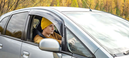 Man in yellow hat and sweater is driving a car along the autumn forest road. Concept of nature, travel and autumn mood.の写真素材
