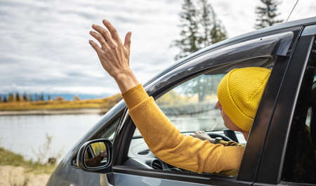 Man in yellow hat and sweater is driving a car along the river and the beautiful autumn forest. Concept of nature, travel and autumn moodの写真素材