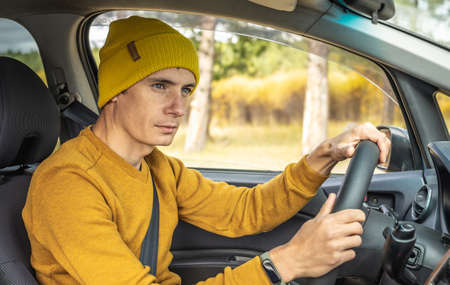 Man in yellow hat and sweater is driving a car along the autumn forest road. Concept of nature, travel and autumn mood.の写真素材