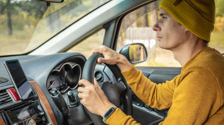 Man in yellow hat and sweater is driving a car along the autumn forest road. Concept of nature, travel and autumn mood.の写真素材