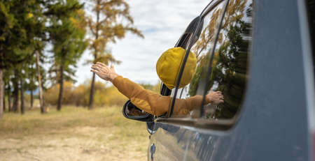 Man is driving a car along a river and forest, leaning out of the car window and stretching his hand up, enjoying the silence, sunlight and beautiful autumn nature. Concept of autumn moodの写真素材