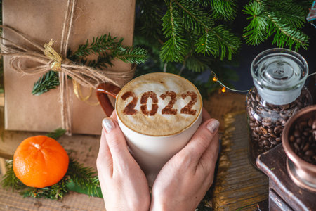 A mug of cappuccino coffee with numbers 2022 on a wooden background with green branches of a...