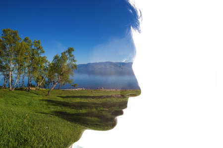 Combination of a silhouette of a face and a landscape with trees, grass, sky and water. Concept of the connection between man and natureの写真素材