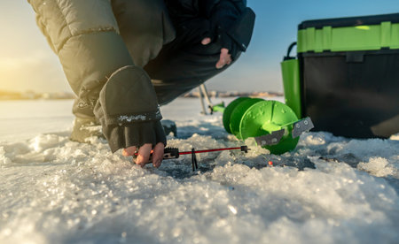 Fisherman is fishing in a hole on a large frozen lake on a sunny day. The joy of winter fishing.