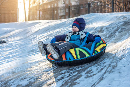 A happy child with his mother is tubing with a park from a slide. A fun winter weekend in the park outside.の写真素材