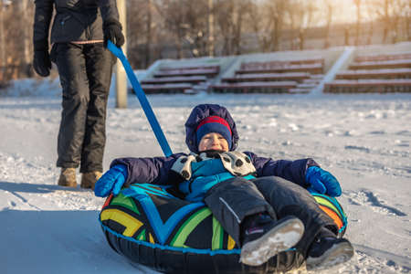 A happy child with his mother is tubing with a park from a slide. A fun winter weekend in the park outside.の写真素材
